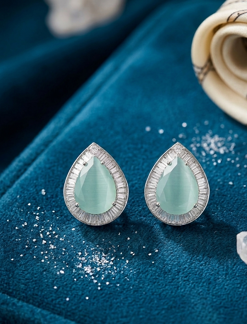 Teardrop-shaped earrings with light green gemstones on a blue fabric background