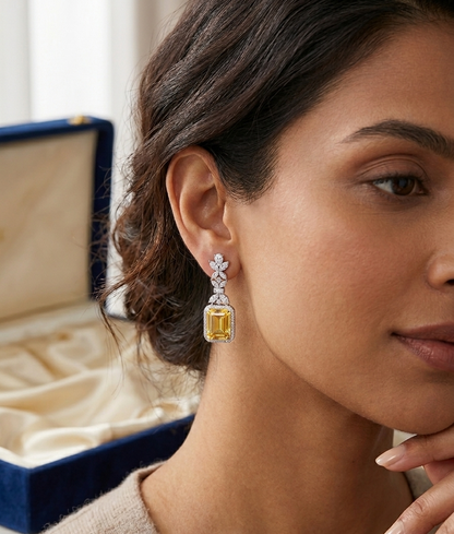 Woman wearing a pair of diamond and yellow gemstone earrings with an open jewelry box in the background.
