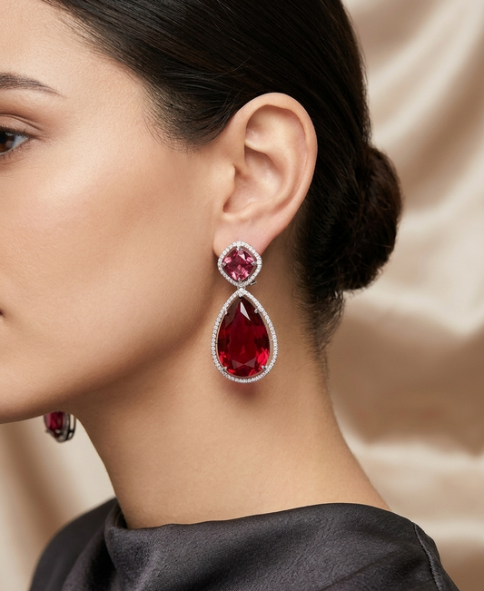 Close-up of a woman wearing red teardrop earrings with a beige background