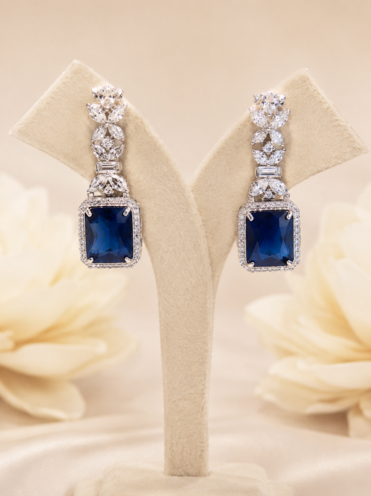 Pair of blue gemstone earrings on a beige stand with floral background