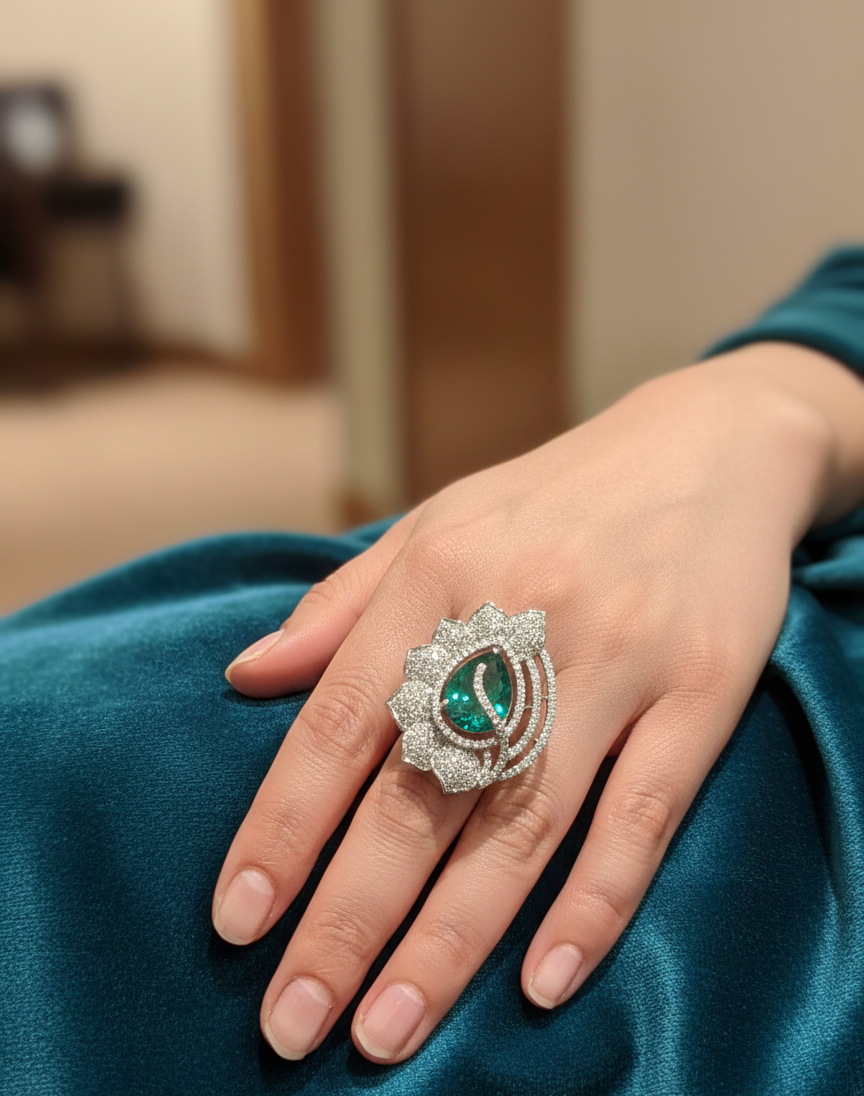 Hand wearing a decorative ring with a green gemstone on a teal fabric background
