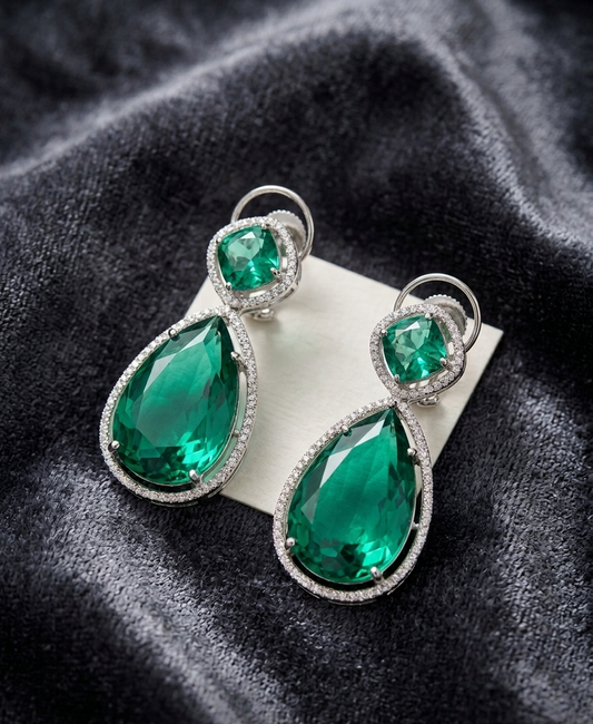 Pair of emerald green teardrop earrings with silver accents on a dark fabric background
