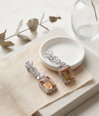 Pair of ornate earrings with orange gemstones on a white surface.