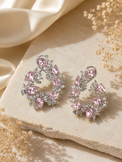 Pair of pink gemstone earrings on a beige stone surface with dried flowers.