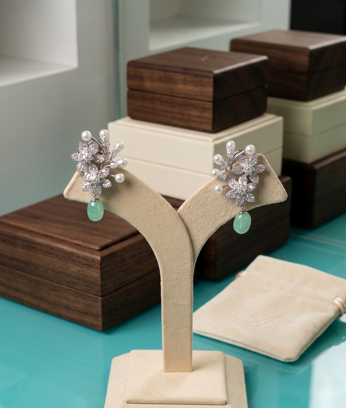 Pair of silver earrings with green gemstones on a beige stand against a display background.