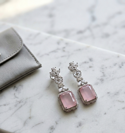 Pink gemstone earrings with silver accents on a marble surface