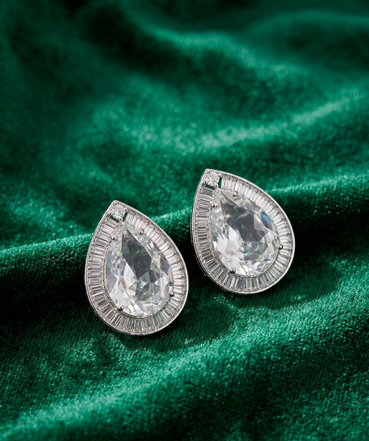 Teardrop-shaped silver earrings with clear gemstones on a green fabric background