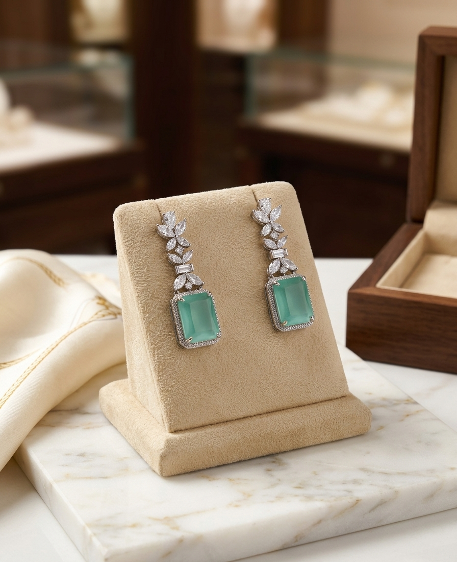Pair of earrings with green gemstones on a beige display stand.