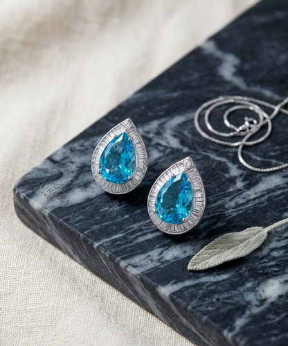 Teardrop-shaped blue gemstone earrings on a dark marble surface with a necklace.