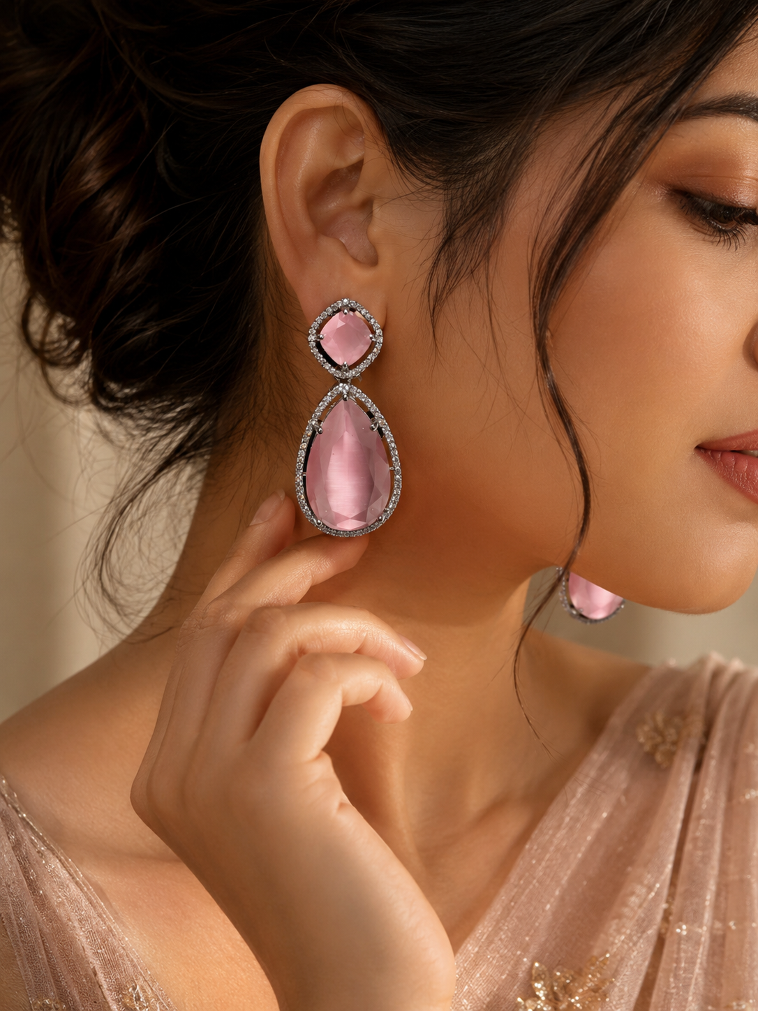 A close-up lifestyle shot of a woman wearing a pair of pink teardrop dangle earrings with silver-toned settings and small clear stones.